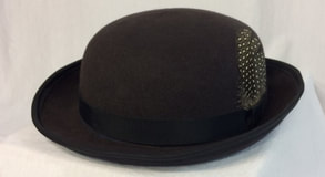 The bowler hat was first seen in London in 1849.  This version has a short crown and rolled wired brim.  It is made of grey wool felt and has a grosgrain band with guinea feathers.  